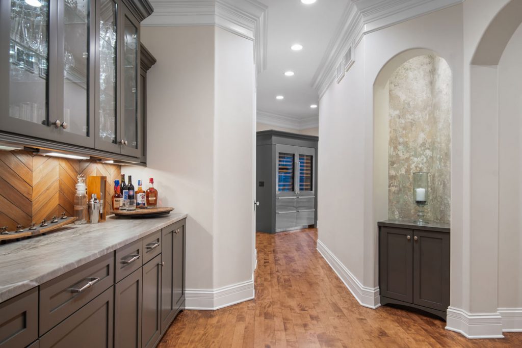 new transformation of hallway leading from kitchen to living room- freshly painted darker cabinets, white walls and updated wood flooring