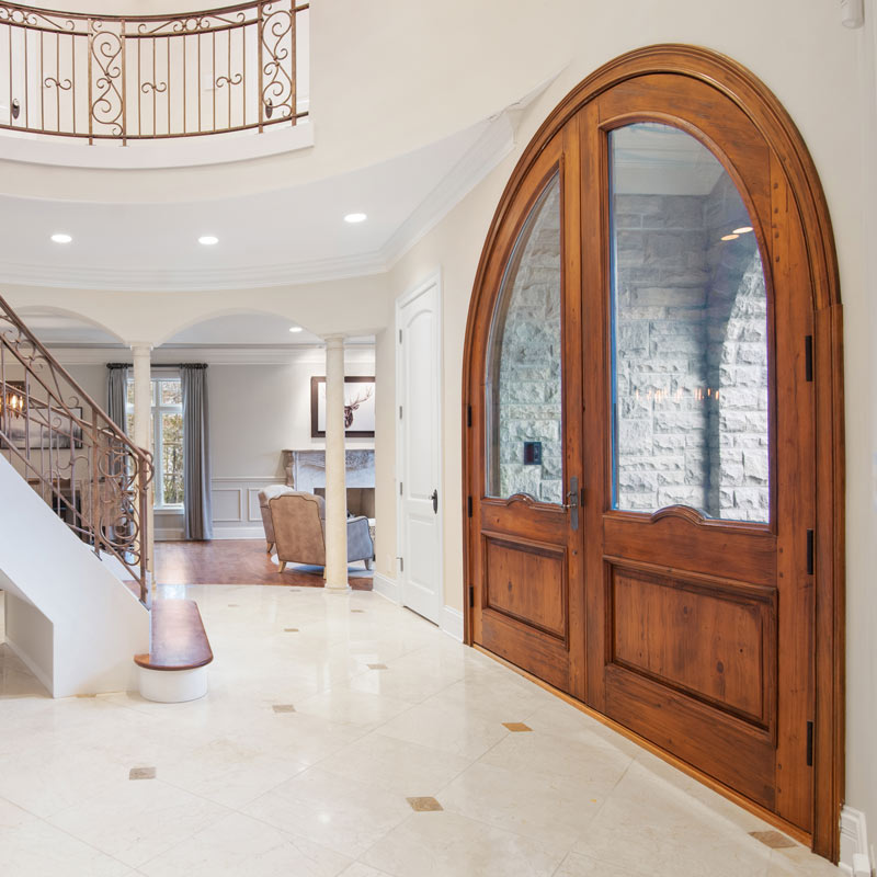 entry way of a large two front door with wood work and arch. Stairs leading up to higher level